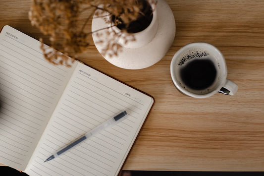A warm cup of coffee beside an open notebook on a table, styled for a calm morning journaling session